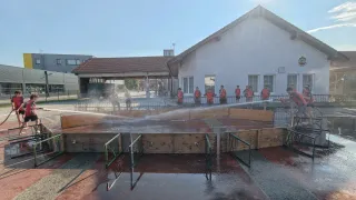 Eine Gruppe von Menschen in roten Uniformen steht neben einem Gebäude. Sie stehen neben einem großen Pool, aus dem Wasser spritzt. Ein Fahrzeug ist im Hintergrund.