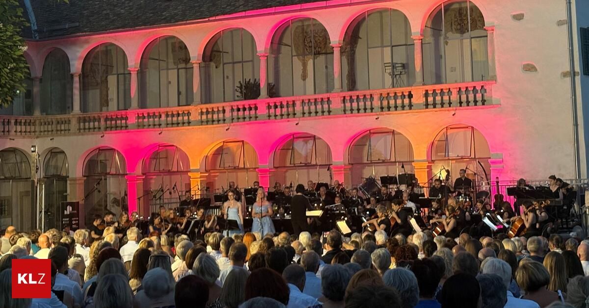Ein Orchester tritt auf einer Bühne vor einem Publikum unter rosa Beleuchtung auf. Zwei Sängerinnen stehen in der Mitte.