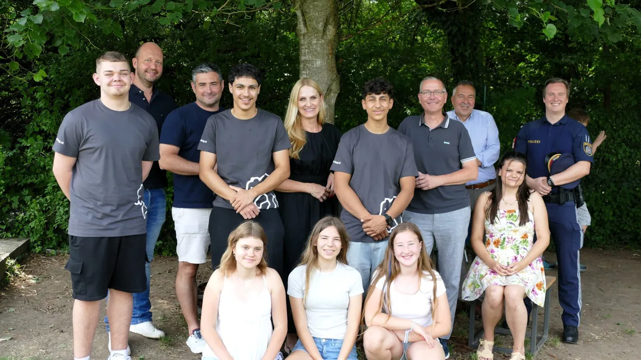 Eine Gruppe von Erwachsenen und Teenagern posiert für ein Foto im Park. Sie alle lächeln und scheinen sich zu amüsieren.