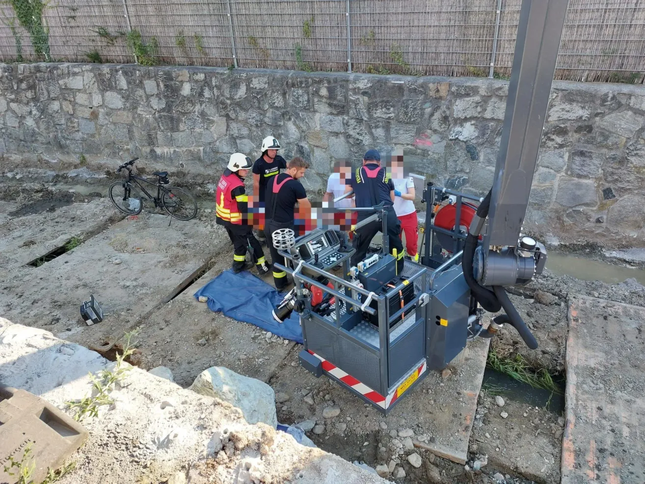 Rettungskräfte stehen um eine Baustelle herum mit einem großen mechanischen Arm und einem Fahrrad auf der linken Seite.