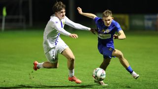 Zwei Fußballspieler spielen auf einem Feld, einer in Weiß und der andere in Blau. Sie versuchen, den Ball zu bekommen.
