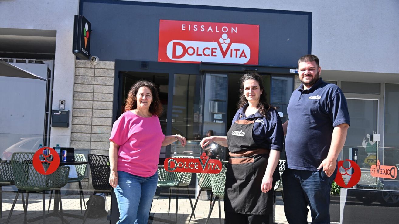Drei Personen stehen vor einem Eissalon namens Dolce Vita. Zwei Frauen lächeln, und ein Mann steht neben ihnen.