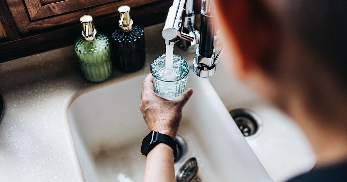 Eine Person füllt ein Glas mit Wasser aus einem Wasserhahn in einer sauberen Küche.