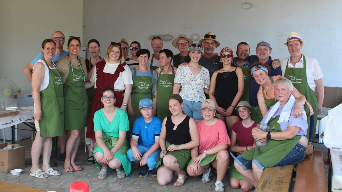 Eine Gruppe von Menschen in grünen Schürzen posiert für ein Foto. Sie tragen verschiedene Accessoires wie Hüte, Brillen und Armbänder. Einige tragen Sandalen, andere Turnschuhe. Einige haben Uhren. Die Wand hinter ihnen ist weiß.