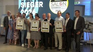 Gruppenfoto der Gewinner eines Wettbewerbs mit einem Banner, das 'SIEGER SALOON 2026' lautet. Die Leute lächeln und halten Urkunden.