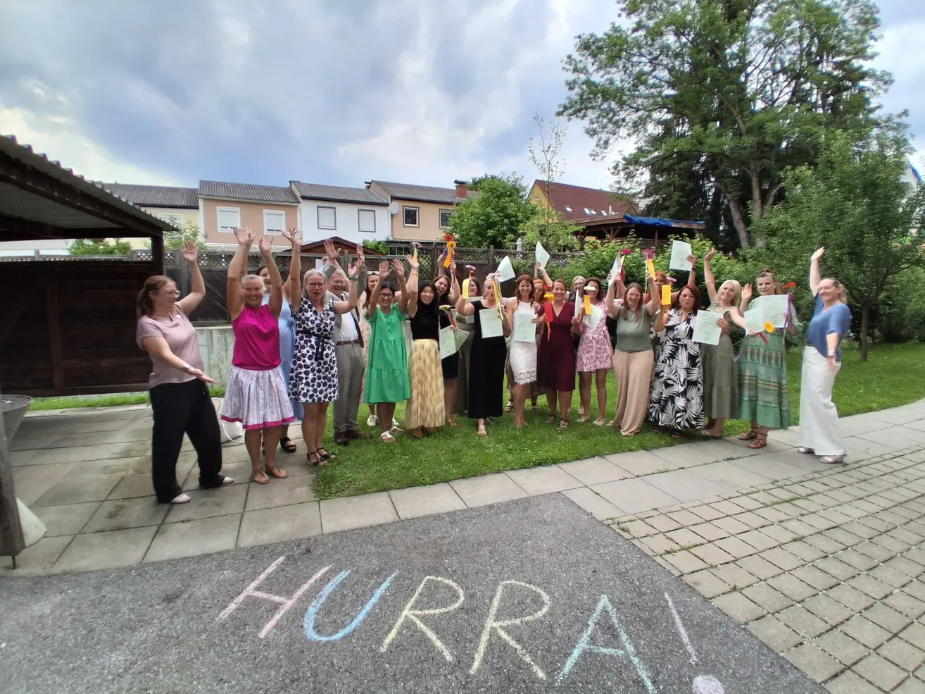 Eine Gruppe von Frauen in Kleidern posiert für ein Foto im Garten mit dem Wort 'Hurra!' auf dem Boden.