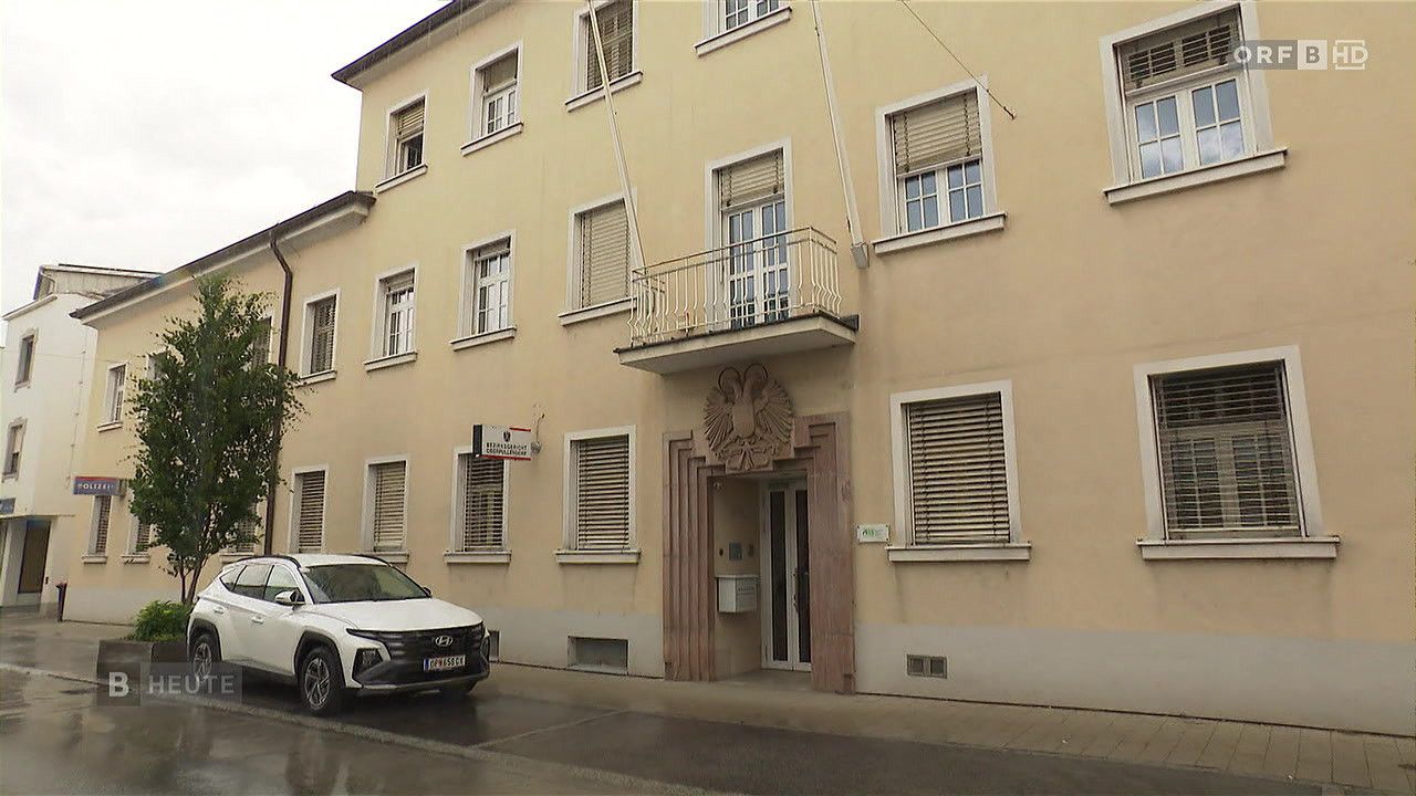 Ein Apartmentgebäude mit Balkonen und einem geparkten Auto davor, mit einem Schild über dem Eingang.