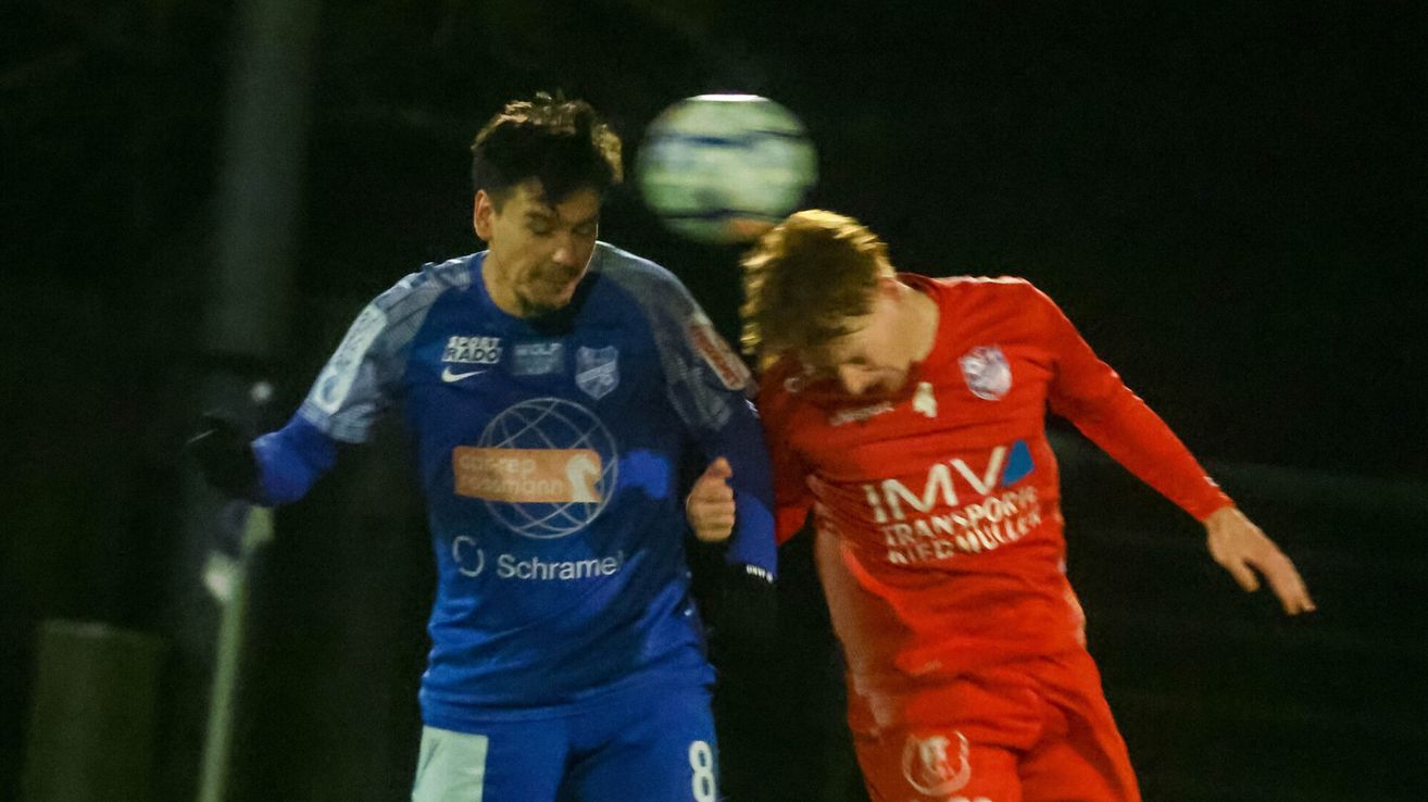Zwei Fußballspieler prallen in der Luft aufeinander. Einer trägt ein blaues Trikot mit 'Schrame' und 'Scott Rado', der andere rot mit 'IMV'. Im Hintergrund befindet sich ein Fußball.
