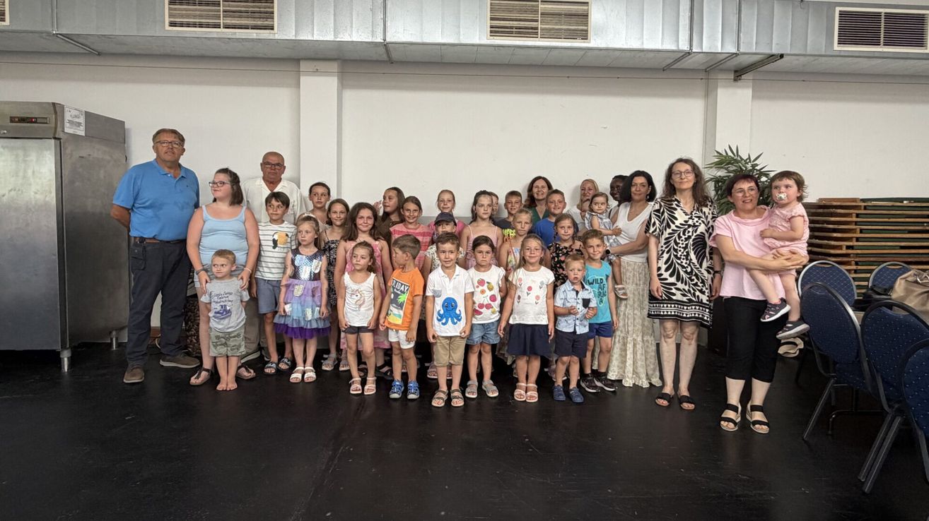 A large group of children and adults are standing together for a group photo in a room.