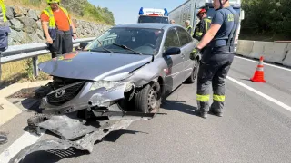 Notfallhelfer stehen neben einem beschädigten Auto. Einer in reflektierender Kleidung inspiziert die Front. In der Nähe geht eine Person in einem Helm am Straßenrand entlang. Dahinter sind Notfallfahrzeuge und ein Geländer sichtbar.