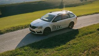 Ein weißer Skoda-Wagen mit dem Wort flux auf der Seite ist auf einer Landstraße geparkt. Die Sonne scheint hell und wirft Schatten auf den Rasen und die Straße.