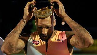 Ein tätowierter Mann hält eine goldene Krone mit der Aufschrift King 100m. Er trägt ein Puma-Trikot. Seine Arme sind erhoben.