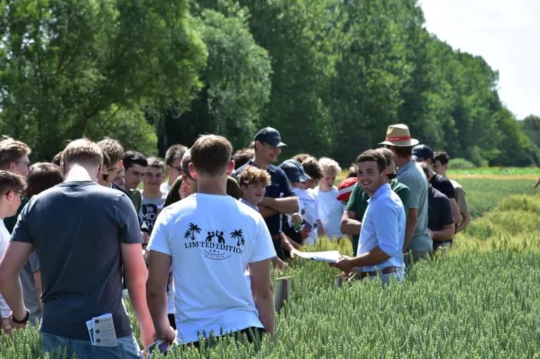 A group of people, including young men and boys, are standing in a field of grass, possibly for an event. Some of them are wearing hats.
