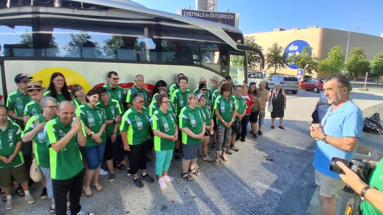 A group of people in green uniforms stands in front of a bus with a sign reading 'Erstmals in Osterreich'. They are likely on a tour.