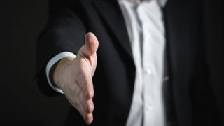 Ein Mann in einem Anzug streckt seine Hand in einer Handschlaggeste aus.