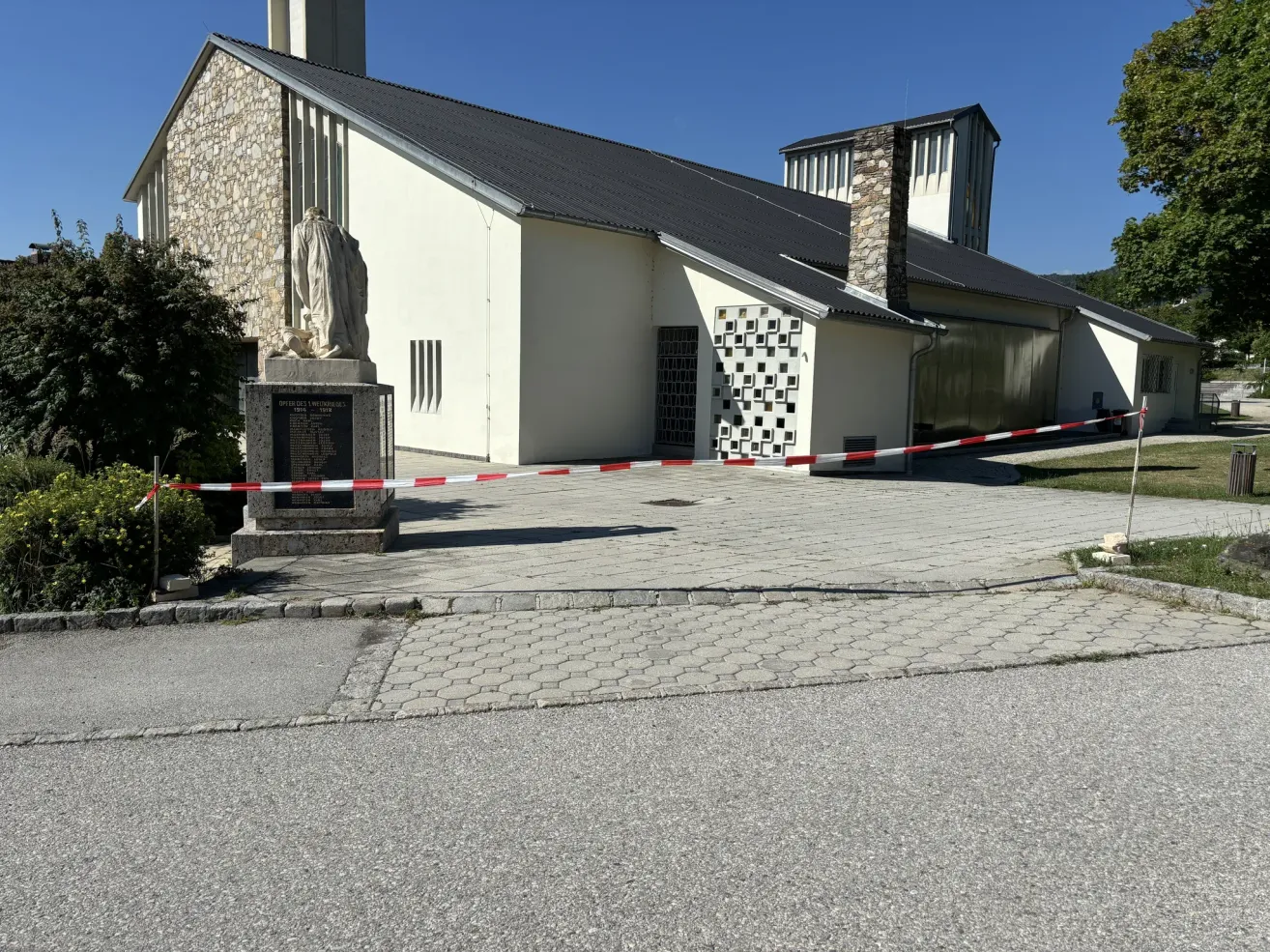Eine moderne Kirche mit einer Statue davor und ein Weg, der von einer Barriere blockiert ist an einem sonnigen Tag.