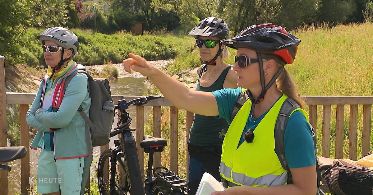 Drei Frauen stehen am Fluss, eine zeigt, trägt Helme und Sonnenbrillen, eine hält eine Karte.