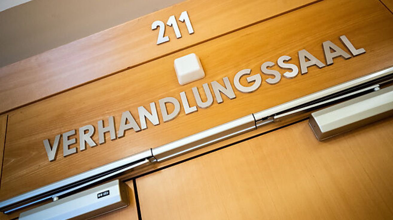 Eine hölzerne Tafel mit weißen Nummern 211 über einer Tür. Die Tür hat einen silbernen Griff.