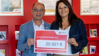 Ein Mann und eine Frau halten ein Zertifikat für Bildungsförderung in der Hand. Der Betrag beträgt 20.921 Euro. Der Mann trägt einen blauen Anzug und die Frau eine Jeansjacke.