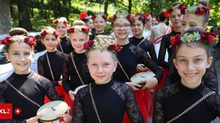 Eine Gruppe junger Mädchen in schwarzen und roten Kleidern, die Tamburine halten und mit Blumenkränzen geschmückt sind, führt einen Tanz im Park auf.