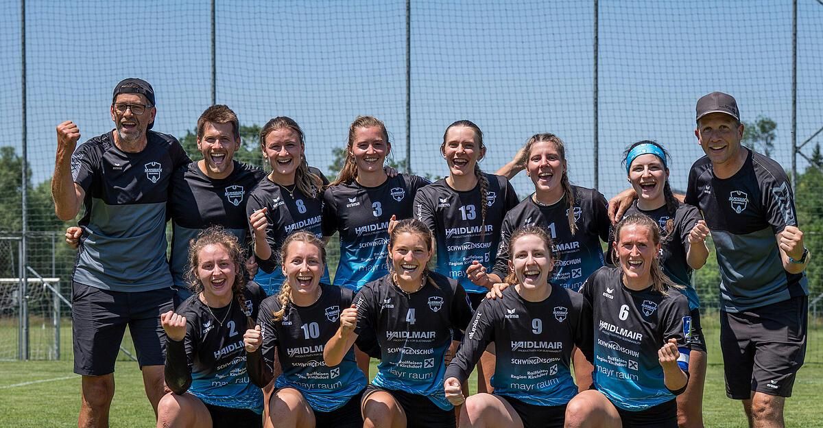 Eine Gruppe von Sportlerinnen in blauen und schwarzen Trikots mit Nummern posiert für ein Foto auf einem Sportplatz.