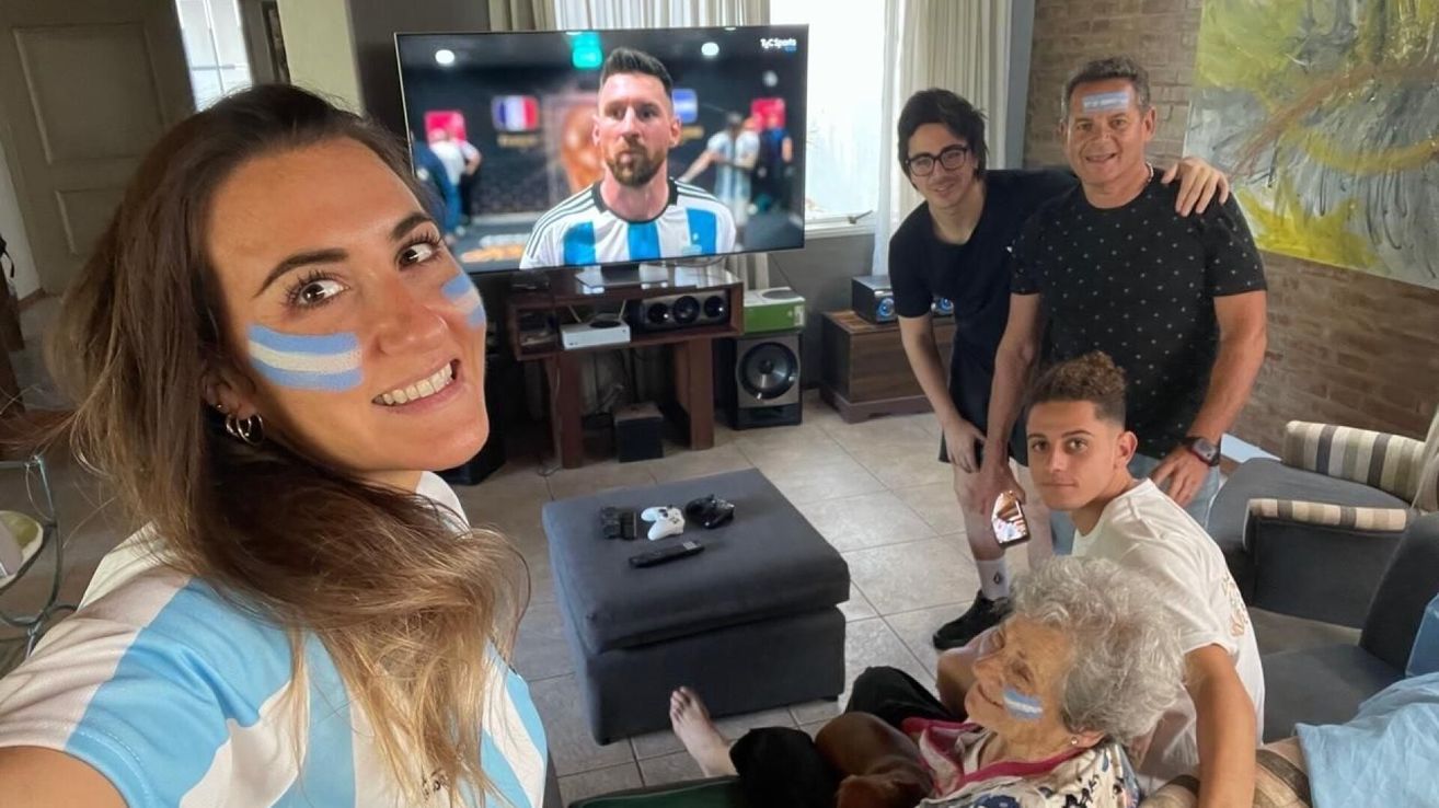 Eine Gruppe von Menschen schaut ein Fußballspiel auf einem großen Fernseher, eine lächelnde Frau und eine andere mit einem Telefon.