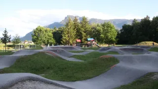 Ein Skatepark mit mehreren Rampen und Hindernissen, umgeben von üppiger Vegetation und Bergen im Hintergrund.