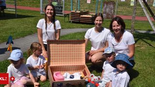 Eine Gruppe von Frauen und Kindern lächelt und posiert für ein Foto. Ein Kind hält einen Kuscheltier. Sie sitzen auf dem Rasen.