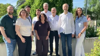 Eine Gruppe von Menschen, einschließlich Männer und Frauen, steht für ein Foto vor einem Baum und einer Betonmauer.