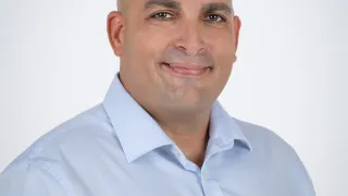 Ein Mann mit kahlem Kopf und hellblauem Hemd lächelt für ein Foto. Das Licht ist auf ihn gerichtet.