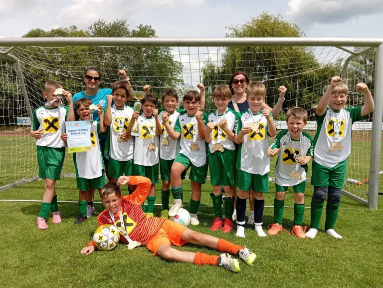 Eine Fußballmannschaft junger Jungen in grünen und weißen Trikots, einige mit Medaillen, posiert für ein Foto auf einem Fußballfeld.