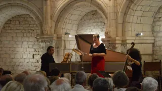 Eine Frau singt vor einem Publikum, während ein Mann hinter ihr Klavier spielt. Sie führen beide in einem historischen Veranstaltungsort auf, mit einer Steinmauer im Hintergrund.