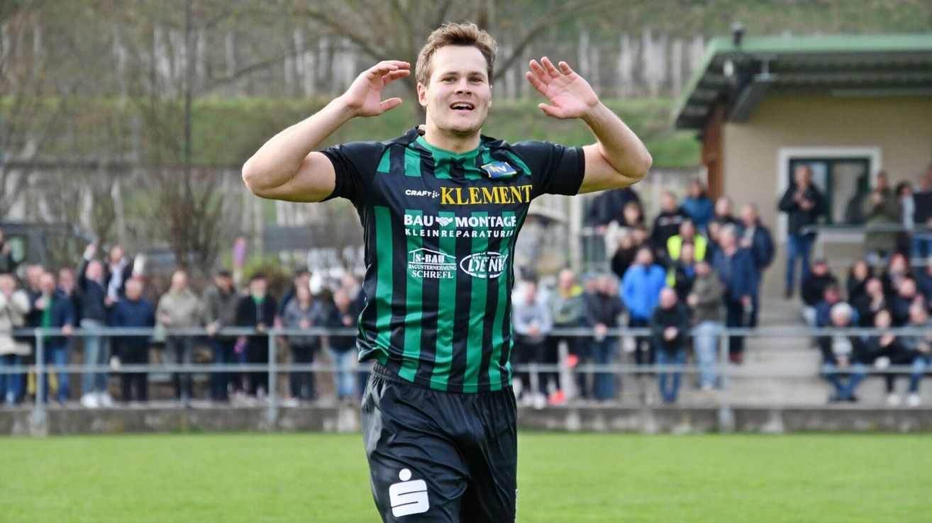 Ein Fußballspieler in einem grün-schwarz gestreiften Trikot feiert ein Tor auf dem Feld. Hinter ihm beobachtet ein Publikum von den Tribünen aus.