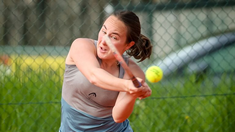Eine Frau in einem Tanktop schlägt einen Tennisball mit einem Schläger, sie konzentriert sich auf den Ball während des Schwungs.