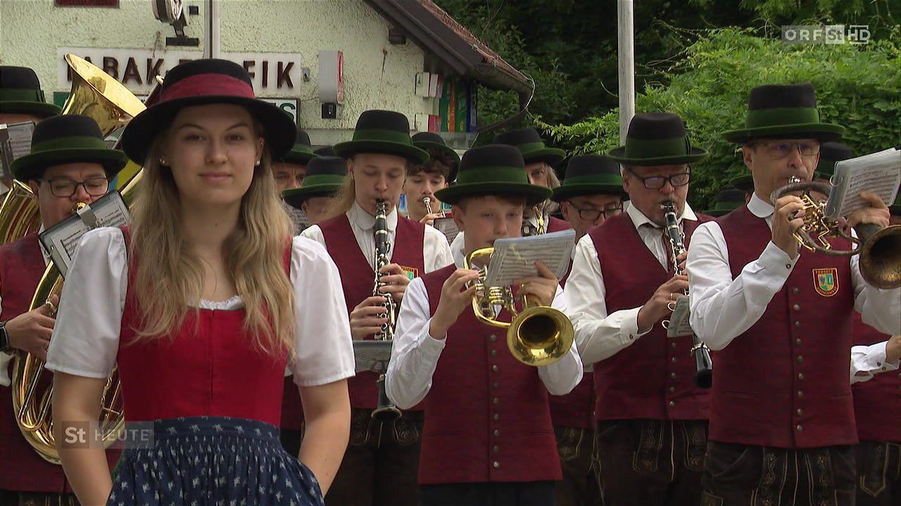Eine Gruppe von Menschen in traditioneller Kleidung mit Hüten spielt Musikinstrumente im Freien vor einem Gebäude.