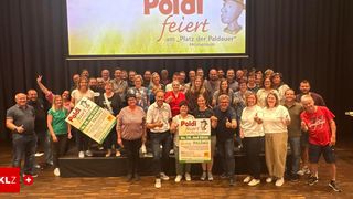 Gruppenfoto von Menschen vor einer Bühne. Sie halten Schilder und lächeln für die Kamera. Ein großes Banner mit der Aufschrift 'Poldifeiert'.