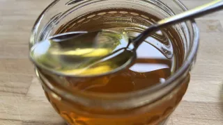 Ein Glas Honig steht auf einer Holzoberfläche. Ein Löffel mit einem Honigtropfen ist im Glas.