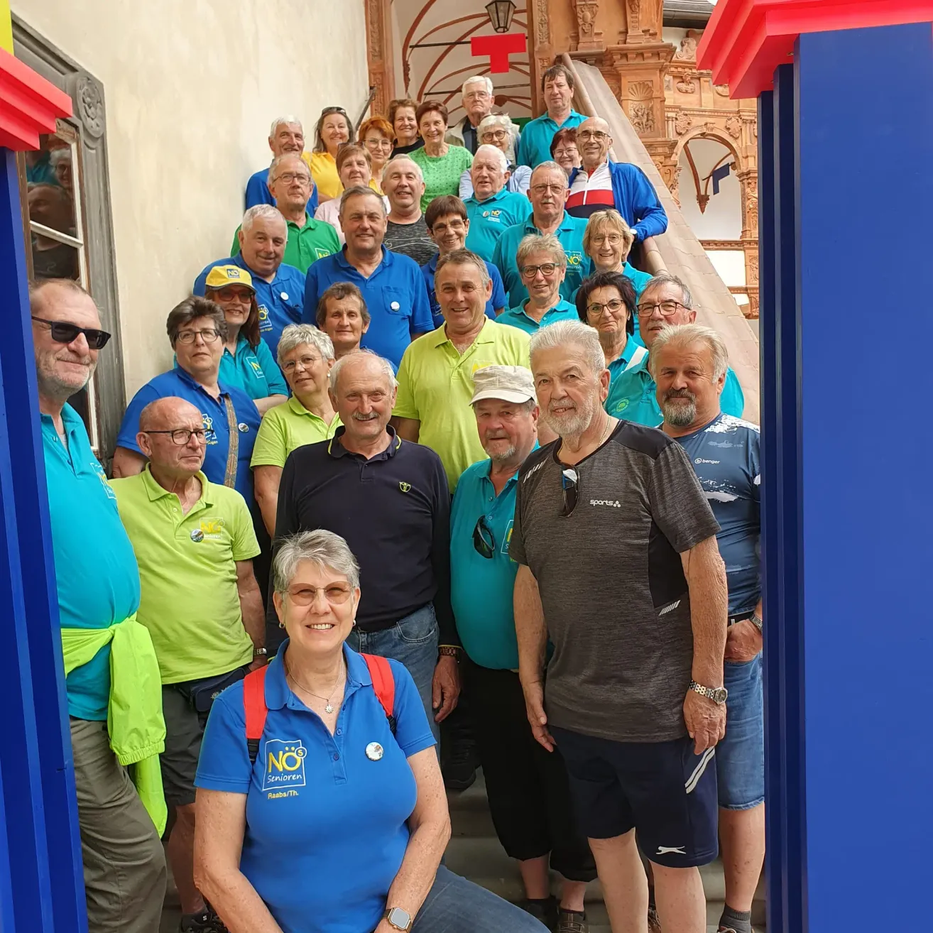 Eine Gruppe von Menschen in unterschiedlich farbigen T-Shirts, einige mit Abzeichen, posiert für ein Foto auf einer Treppe.