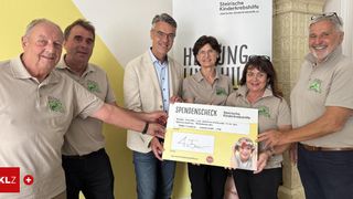 Eine Gruppe von Menschen, die einen Spendenscheck mit der Aufschrift 'Spendenscheck' vor einem Banner mit einem Bild eines Kindes halten.