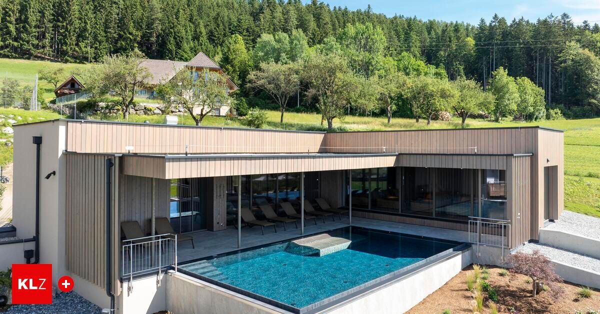 Ein Außenpool in einem luxuriösen modernen Haus mit einer Glasfassade und einer überdachten Terrasse. Bäume und ein Haus im Hintergrund.