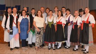 Eine Gruppe von Menschen, bestehend aus Männern und Frauen, gekleidet in traditioneller Kleidung, stehen zusammen und lächeln für ein Foto.