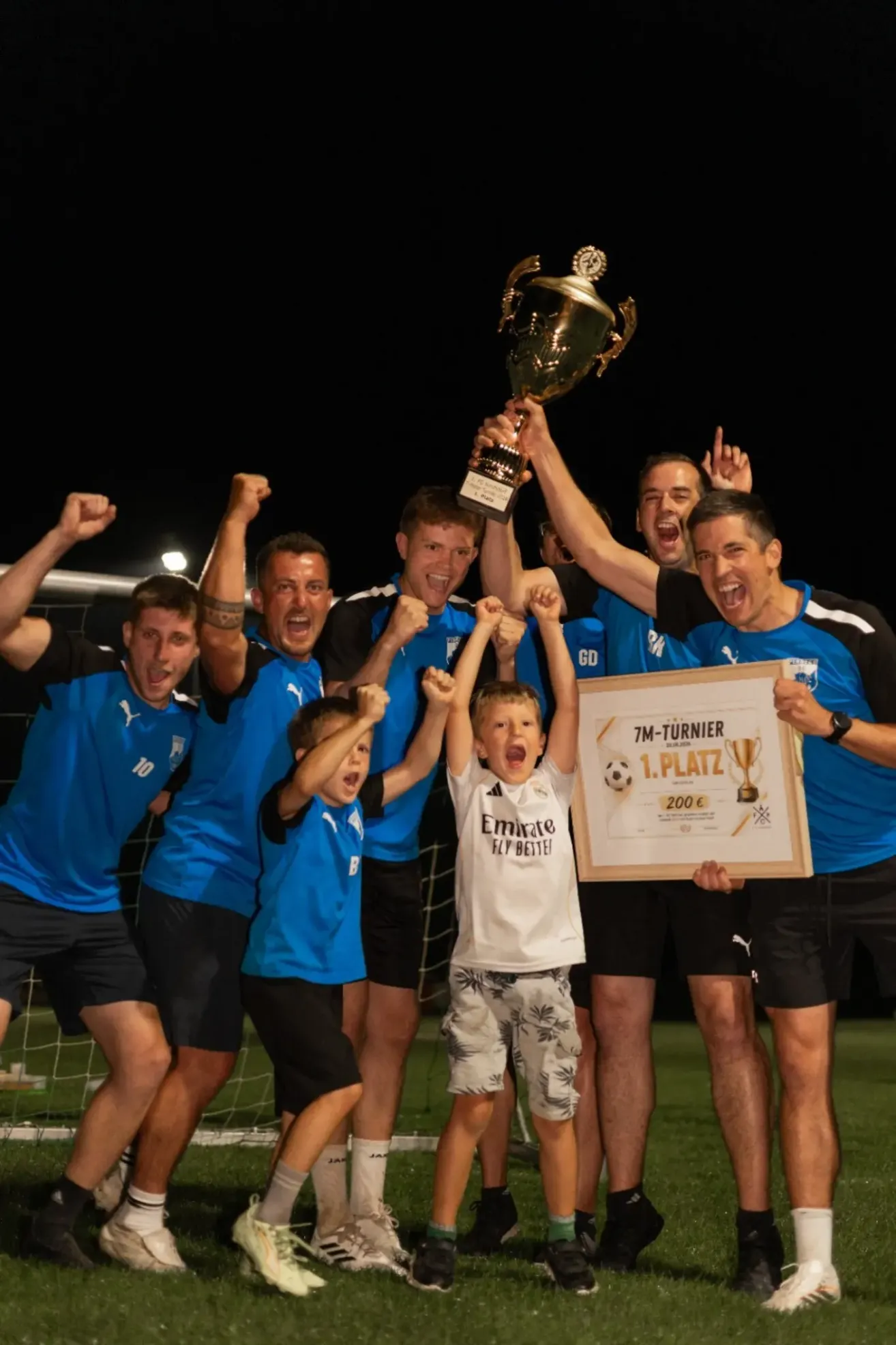 Eine Gruppe von Menschen in blauen Trikots feiert mit einem Pokal und einem Zertifikat. Einige heben die Hände, und ein Kind hält ein Zertifikat.