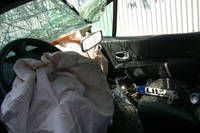 Der Innenraum eines beschädigten Autos zeigt ein ausgelöstes Airbag, ein zerknittertes Lenkrad und einen weißen Stoff, der einen Teil des Armaturenbretts bedeckt.