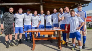 Eine Gruppe männlicher Athleten in einheitlichen Kleidungsstücken posiert für ein Foto mit einer Trophäe auf einem Holztisch vor ihnen.