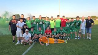 Eine Fußballmannschaft in grünen und roten Trikots posiert für ein Gruppenfoto auf einem Feld. Ein Spieler liegt lächelnd auf dem Boden.