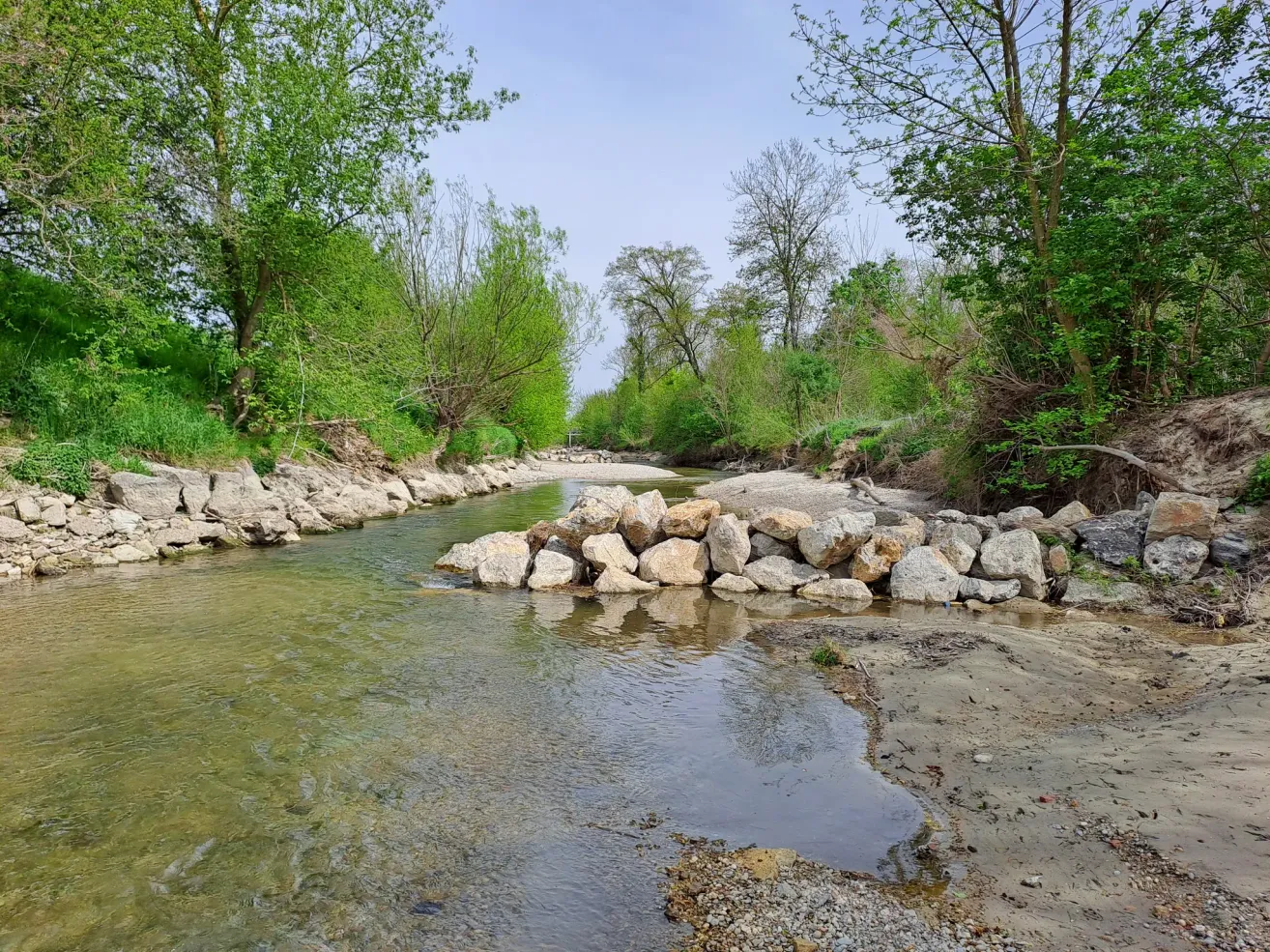 Ein ruhiger Fluss mit klarem Wasser, umgeben von grünen Bäumen und Felsen an einem sonnigen Tag.