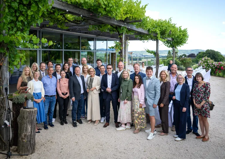 Eine Gruppe von Personen, die formell gekleidet sind, posiert für ein Foto vor einem Gebäude mit viel Grün.