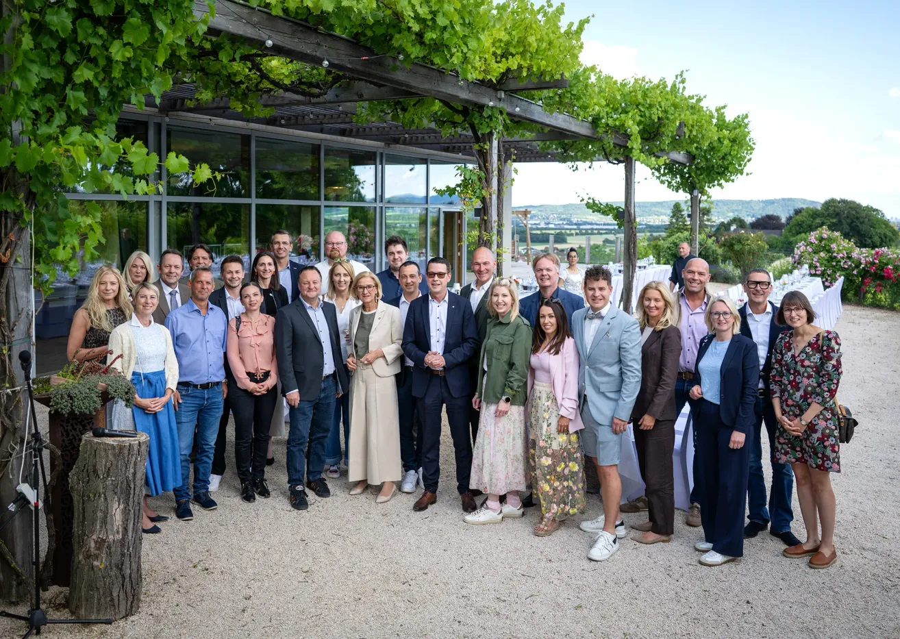 Eine Gruppe von Personen, die formell gekleidet sind, posiert für ein Foto vor einem Gebäude mit viel Grün.