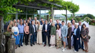 Eine Gruppe von Personen, die formell gekleidet sind, posiert für ein Foto vor einem Gebäude mit viel Grün.