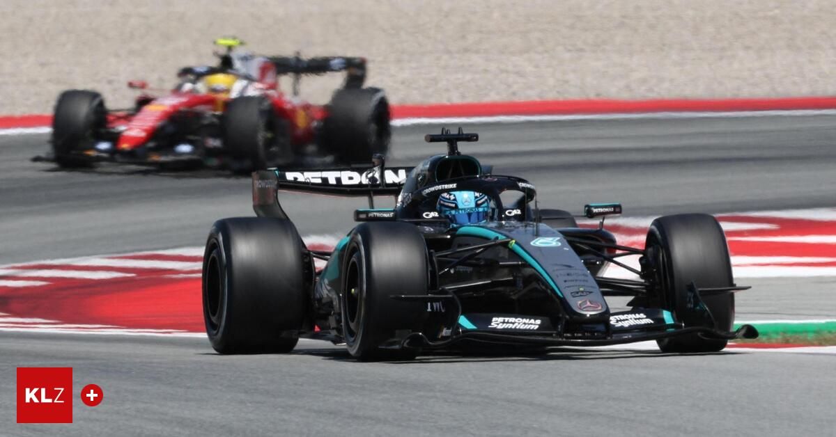 Ein Mercedes Formel-1-Auto fährt auf einer Rennstrecke, mit einem anderen Auto im Hintergrund. Das Auto hat blaue und schwarze Farben und trägt die Petronas-Marke. Der Fahrer trägt einen Helm.